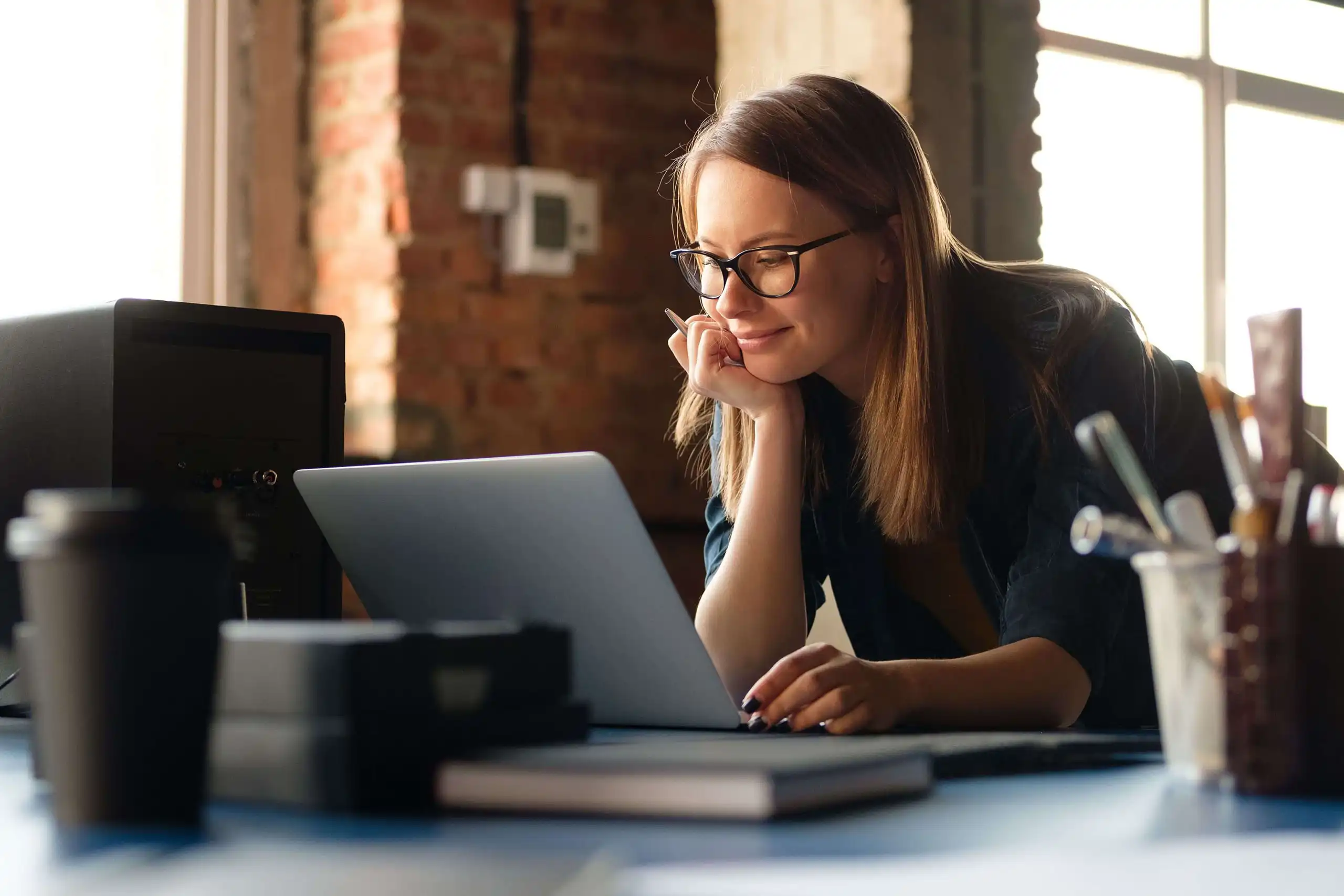 Lady smiling with glasses on and doing work on laptop